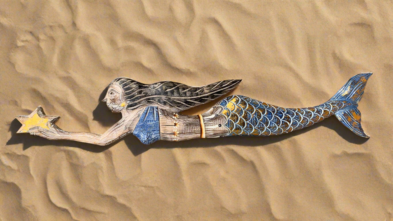 wooden mermaid sculpture with blue tail reaching for a star on the sand