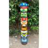 Tall multicolored tiki totem pole with carved faces outdoors.