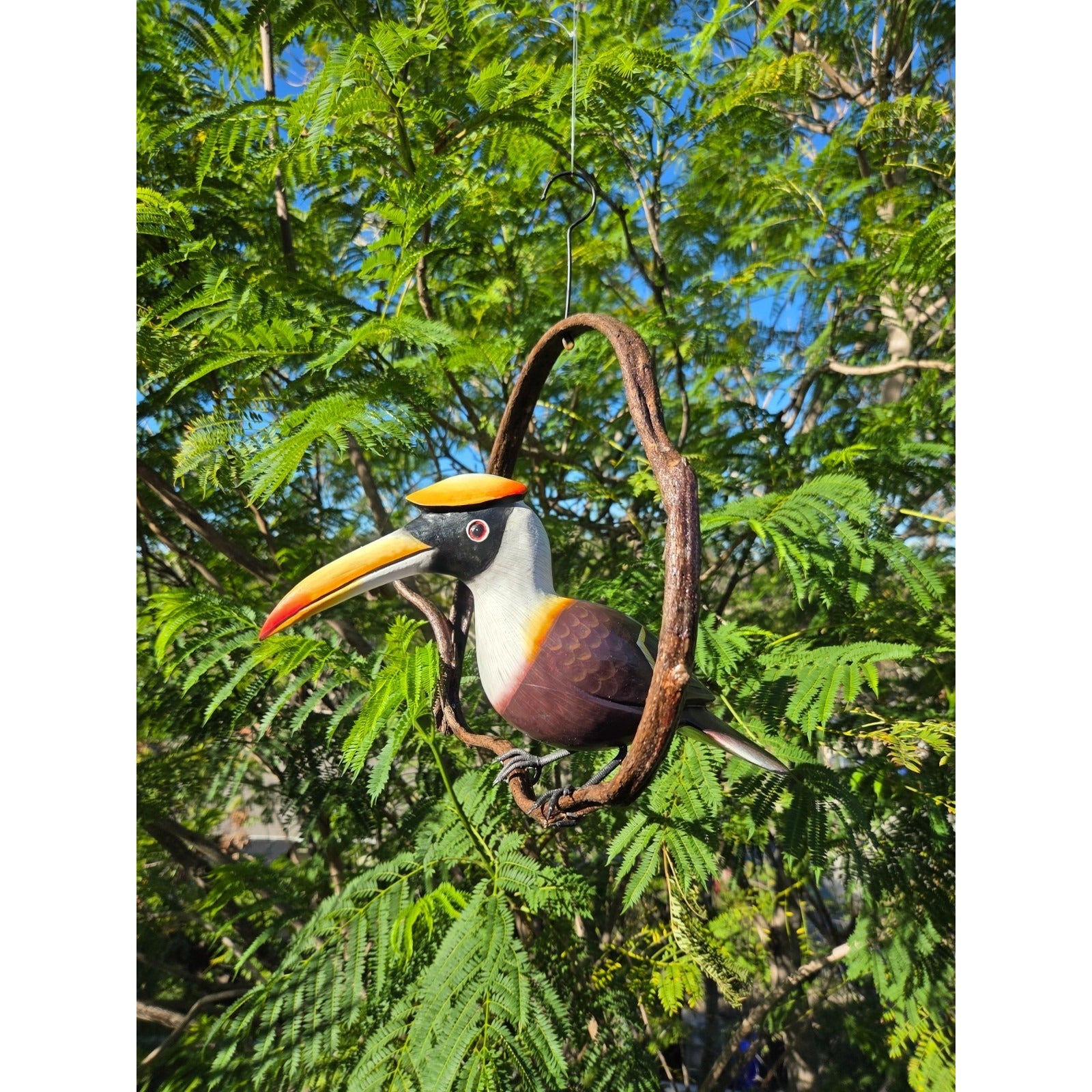 Decorative hornbill bird hanging from a branch with green foliage in the background