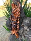 Orange and black wooden carved totem attached to a tree trunk with green leaves in the background.