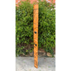 Orange totem pole with black abstract carvings beside a green hedge