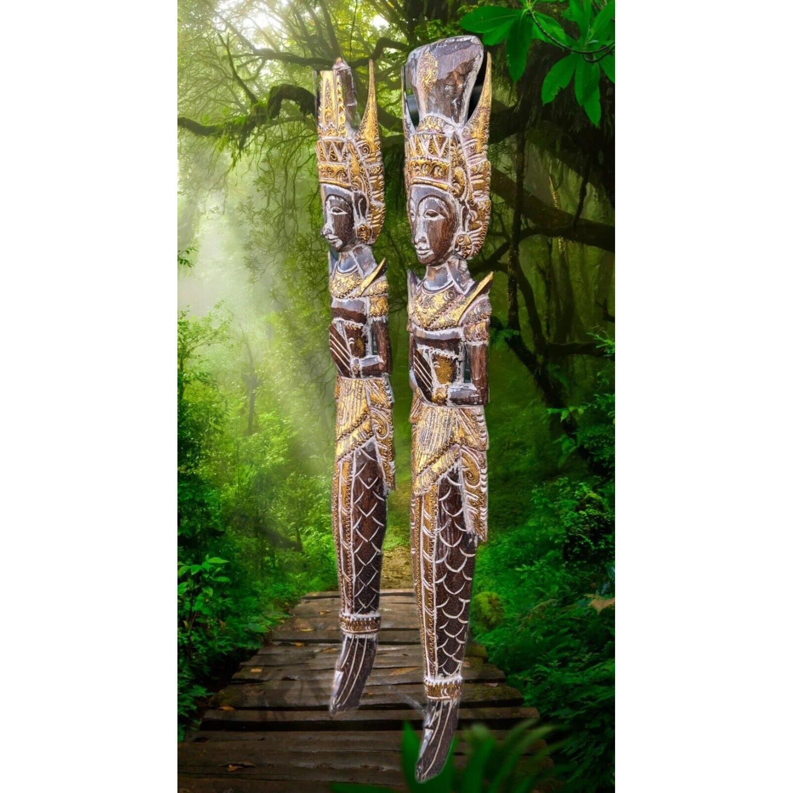 Two ornate carved wooden statues with tall headdresses on a wooden boardwalk in a lush tropical forest
