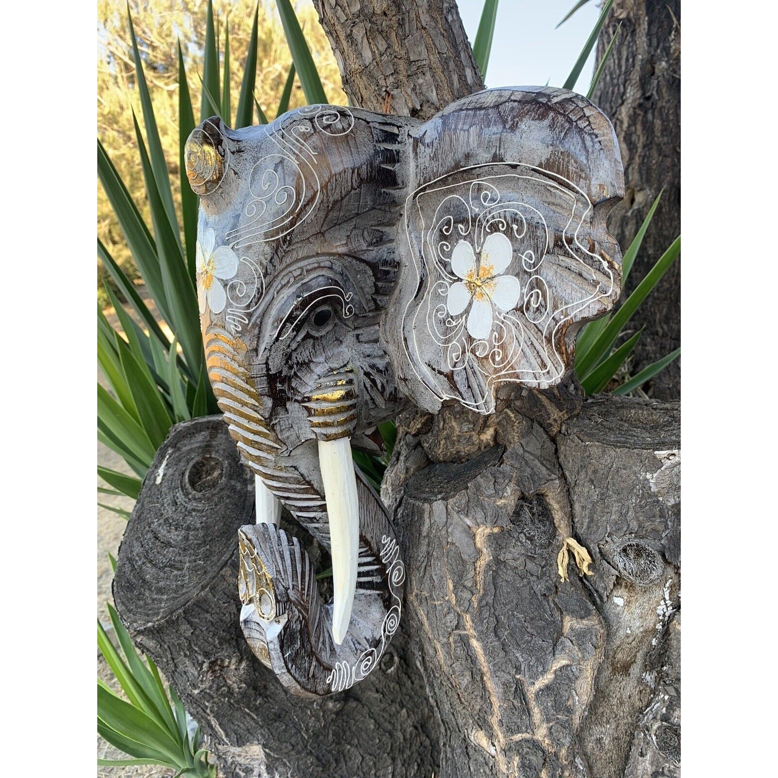 Carved elephant head on a tree trunk with white floral swirl patterns on the ears.
