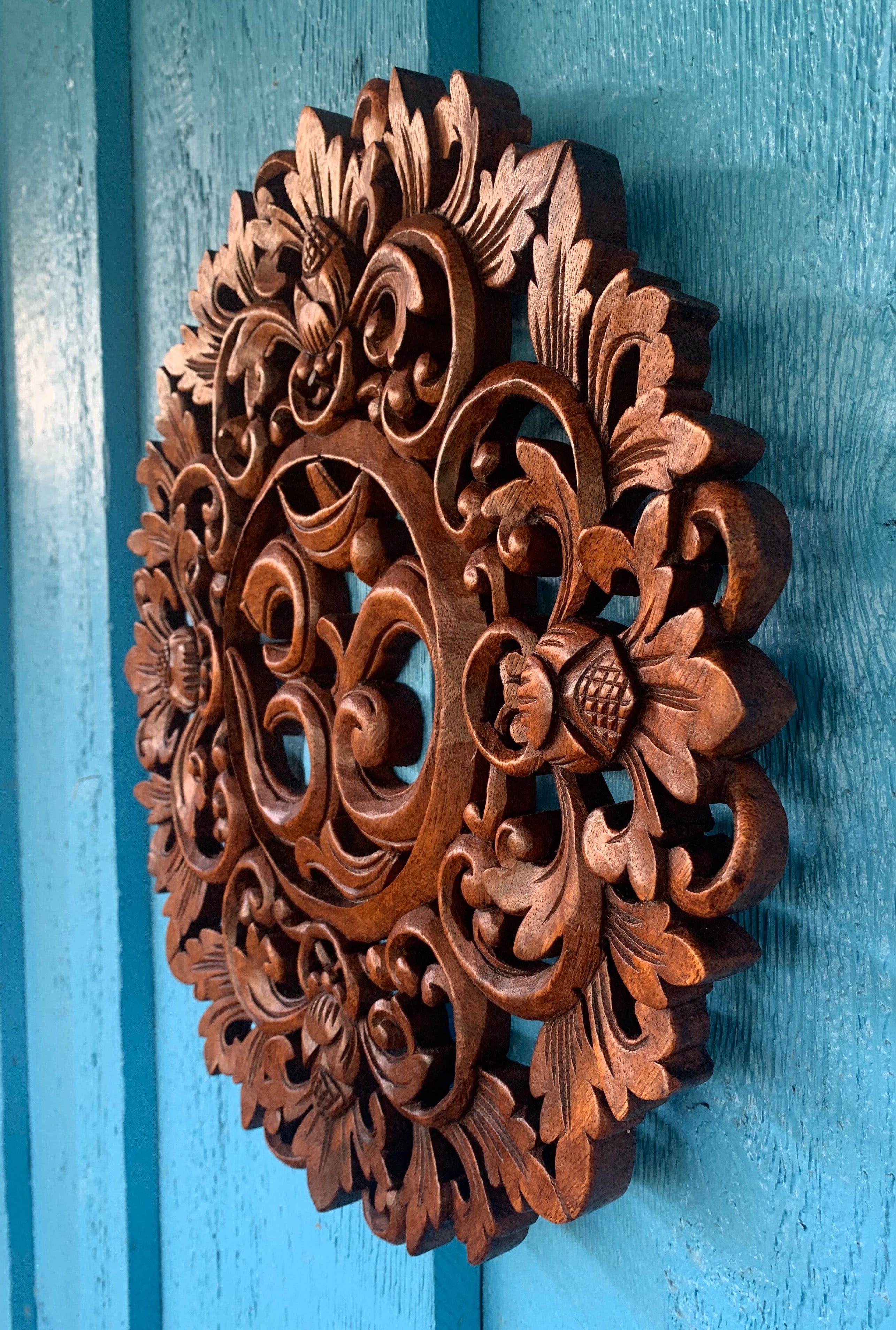 Intricately carved wooden rosette with floral motifs on a turquoise background