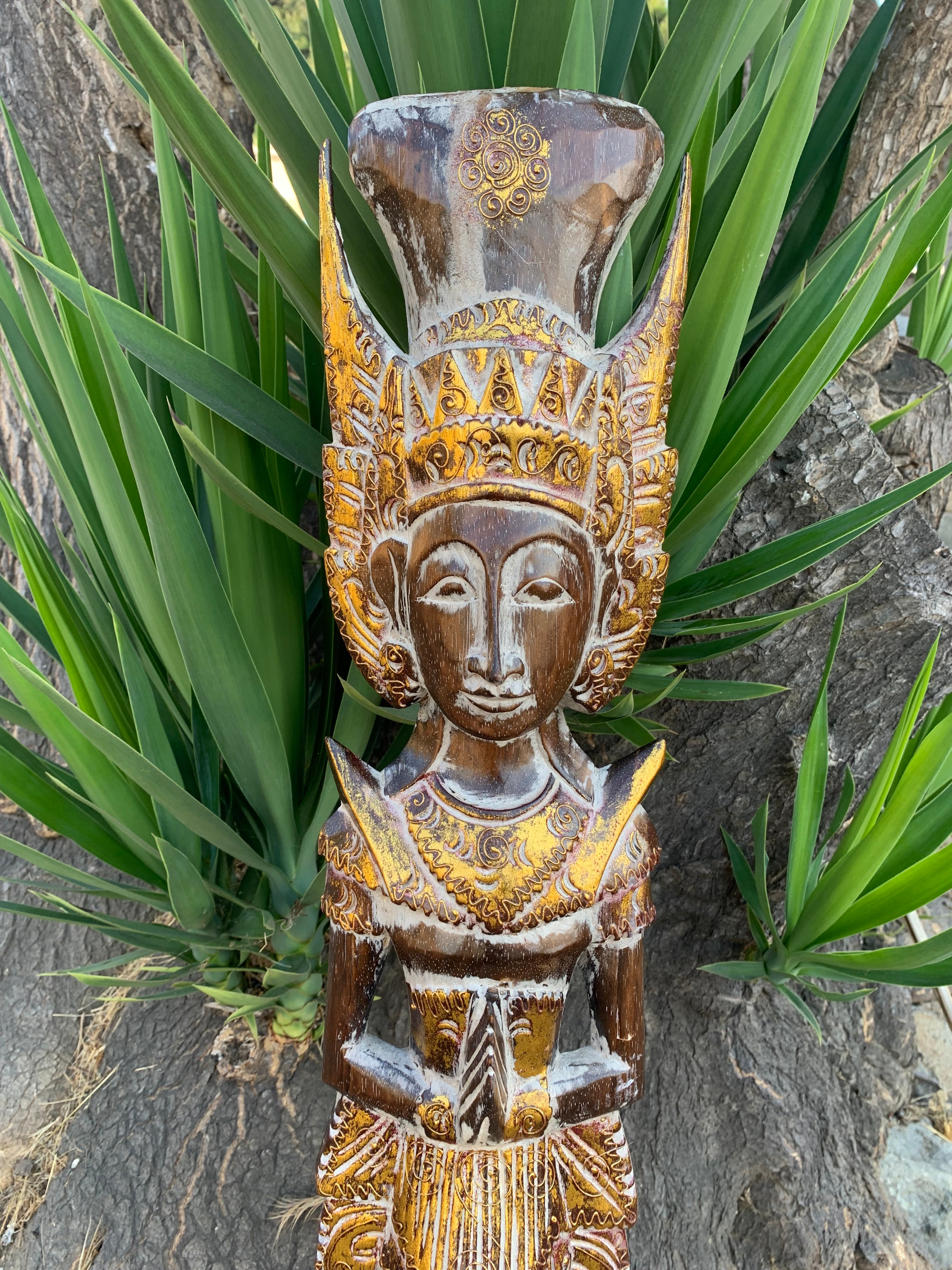 Wooden carved statue with ornate crown and gold detailing among green plants