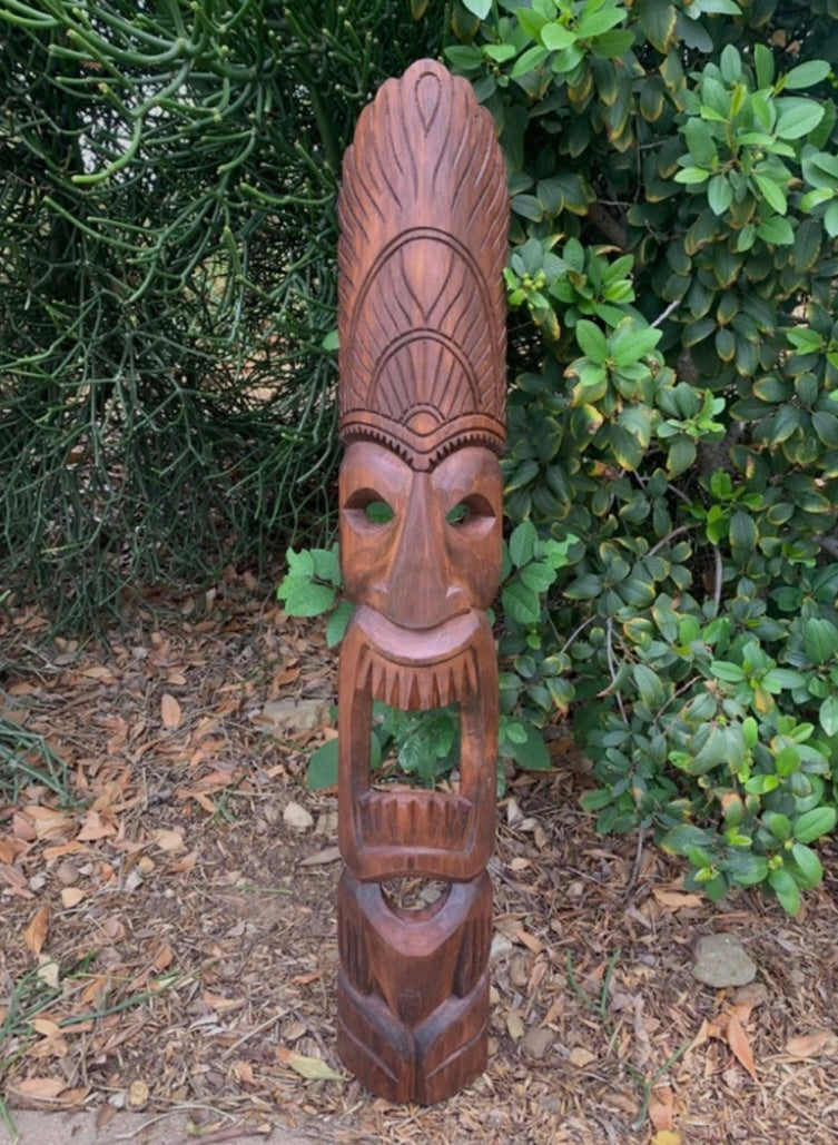 Outdoor wooden tiki carving with elongated headdress and open mouth