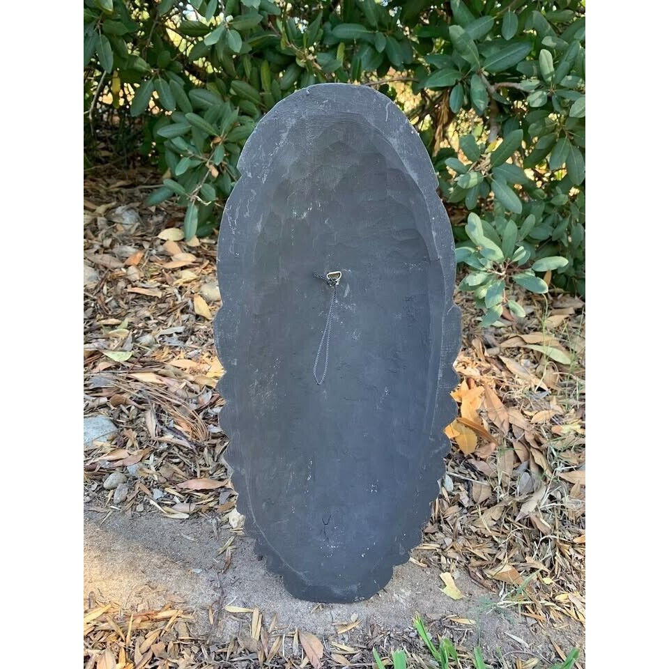 oval slate headstone with rough edges and a hanging loop in an outdoor garden setting