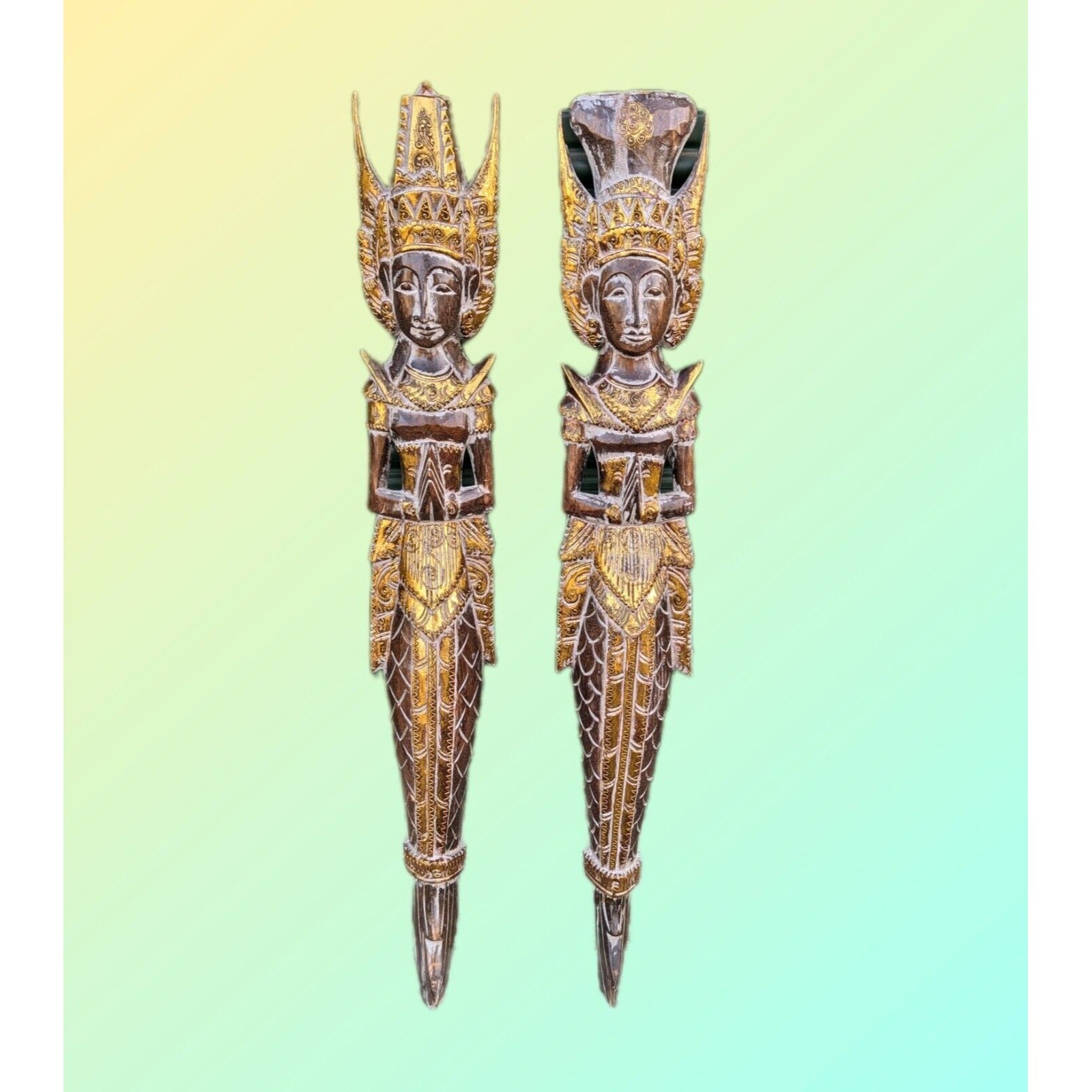 Two gold-toned carved statues with elaborate crowns standing side by side on a pastel gradient background.