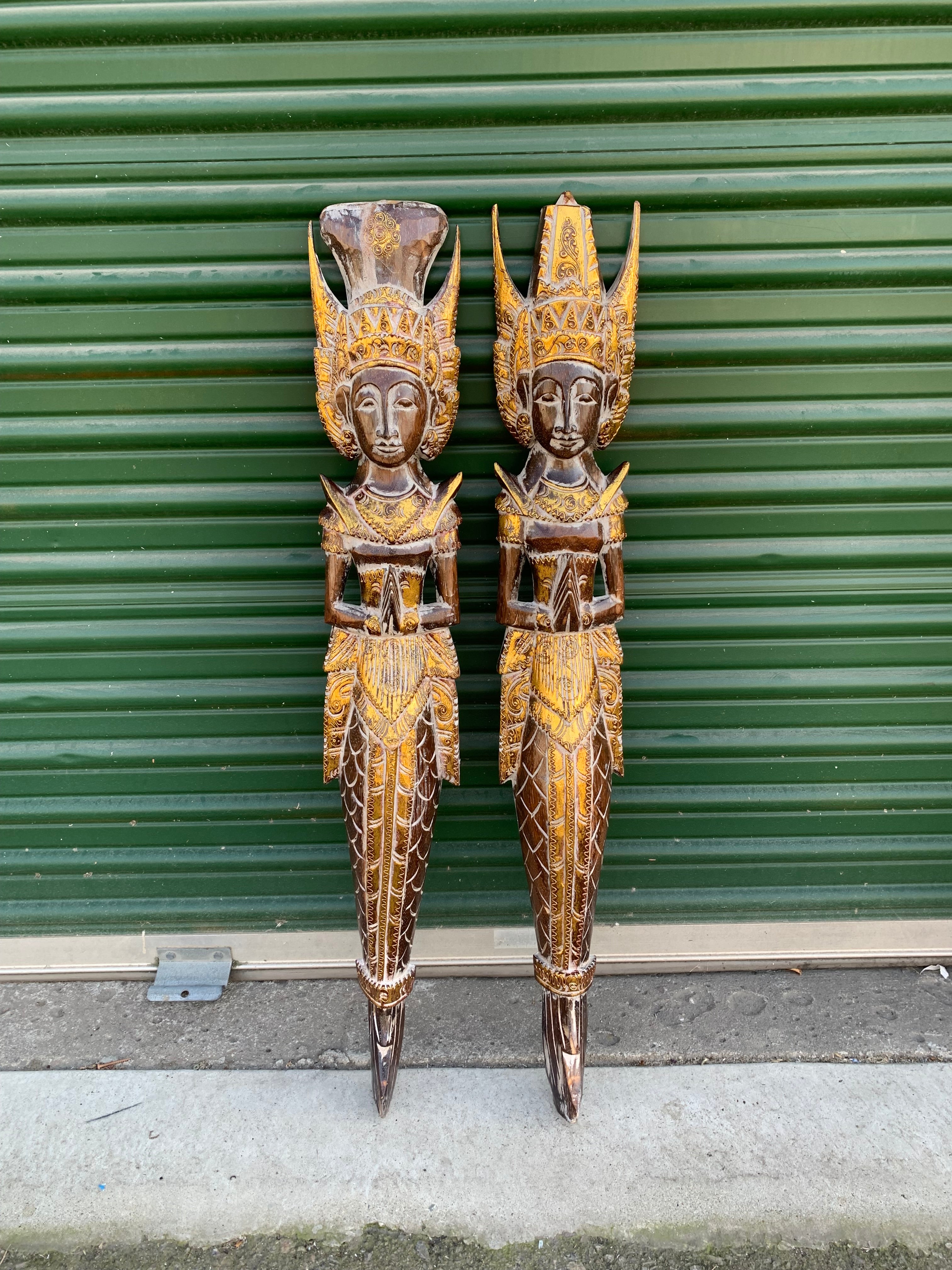 Pair of elaborately carved wooden statues with gold detailing and tall crowns, standing against a green shutter.