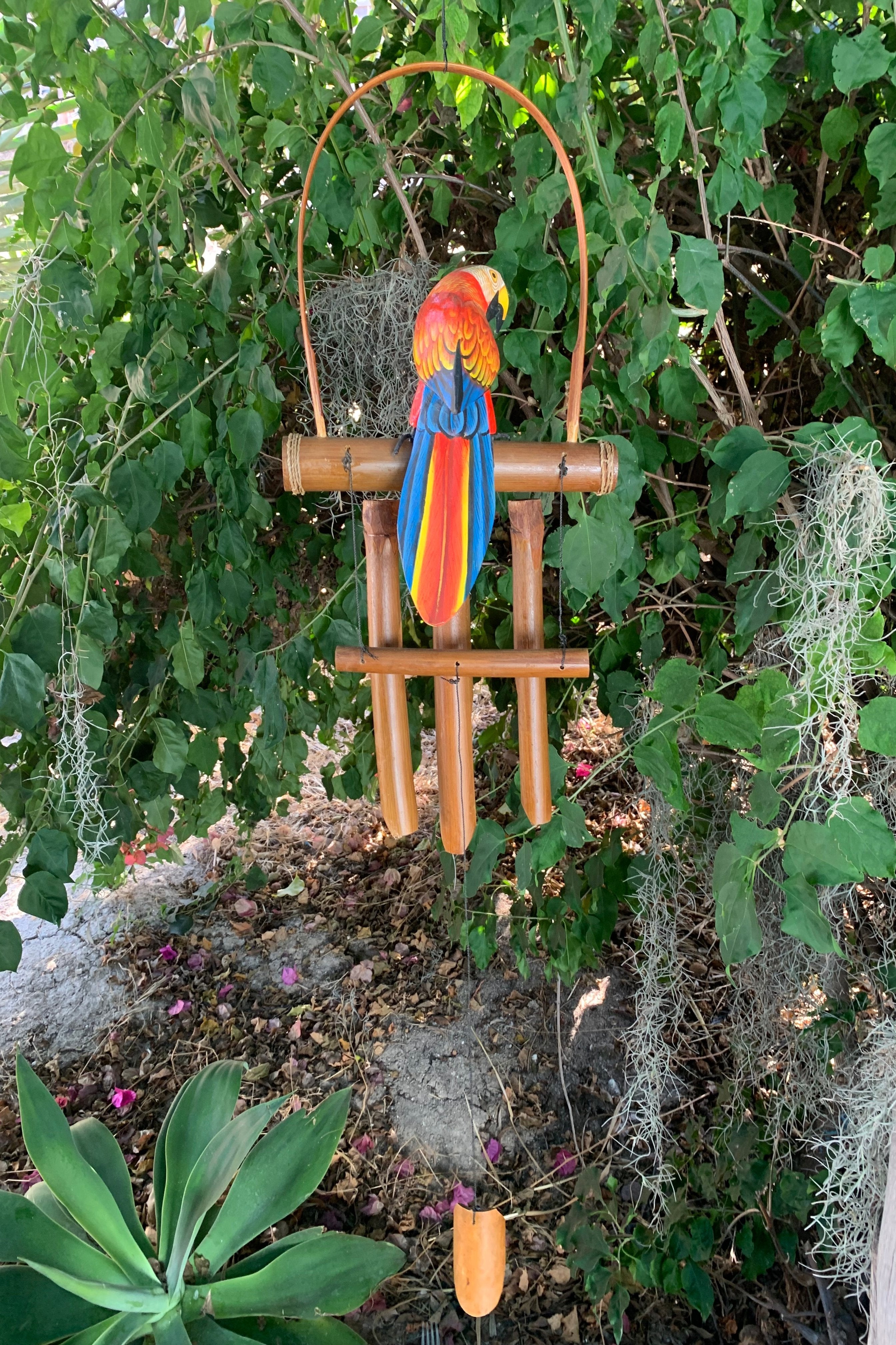 Colorful parrot wind chime hanging from bamboo stand in a leafy garden