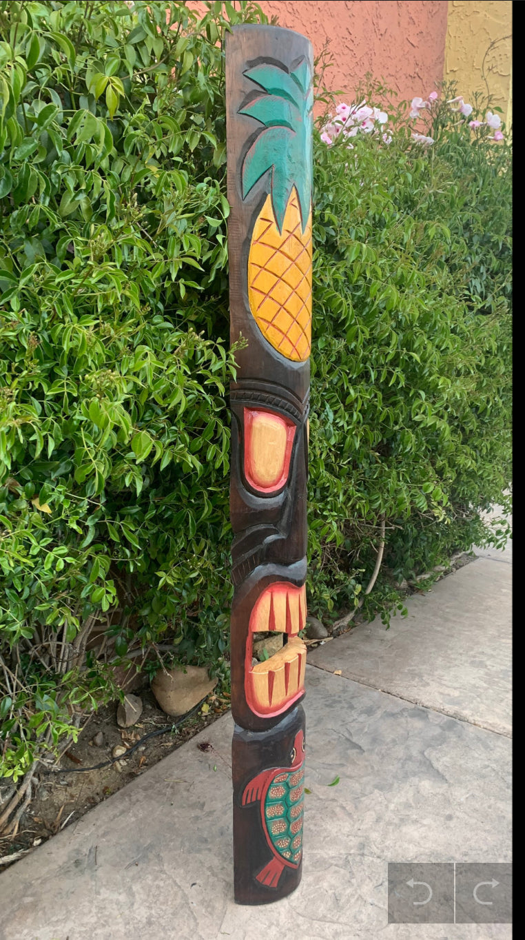 Pineapple-topped wooden tiki totem pole carved in bright colors in a garden