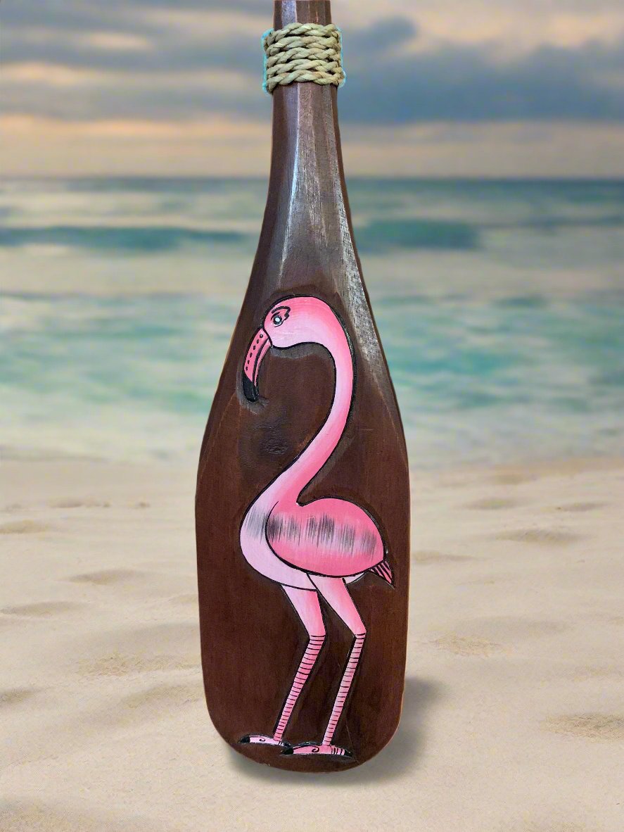 Pink flamingo painting on a brown bottle standing on a sandy beach.