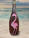 Pink flamingo painting on a brown bottle standing on a sandy beach.