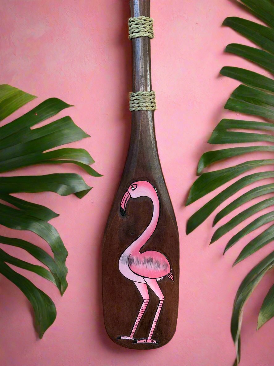 pink flamingo painting on wooden paddle against pink wall with green tropical leaves