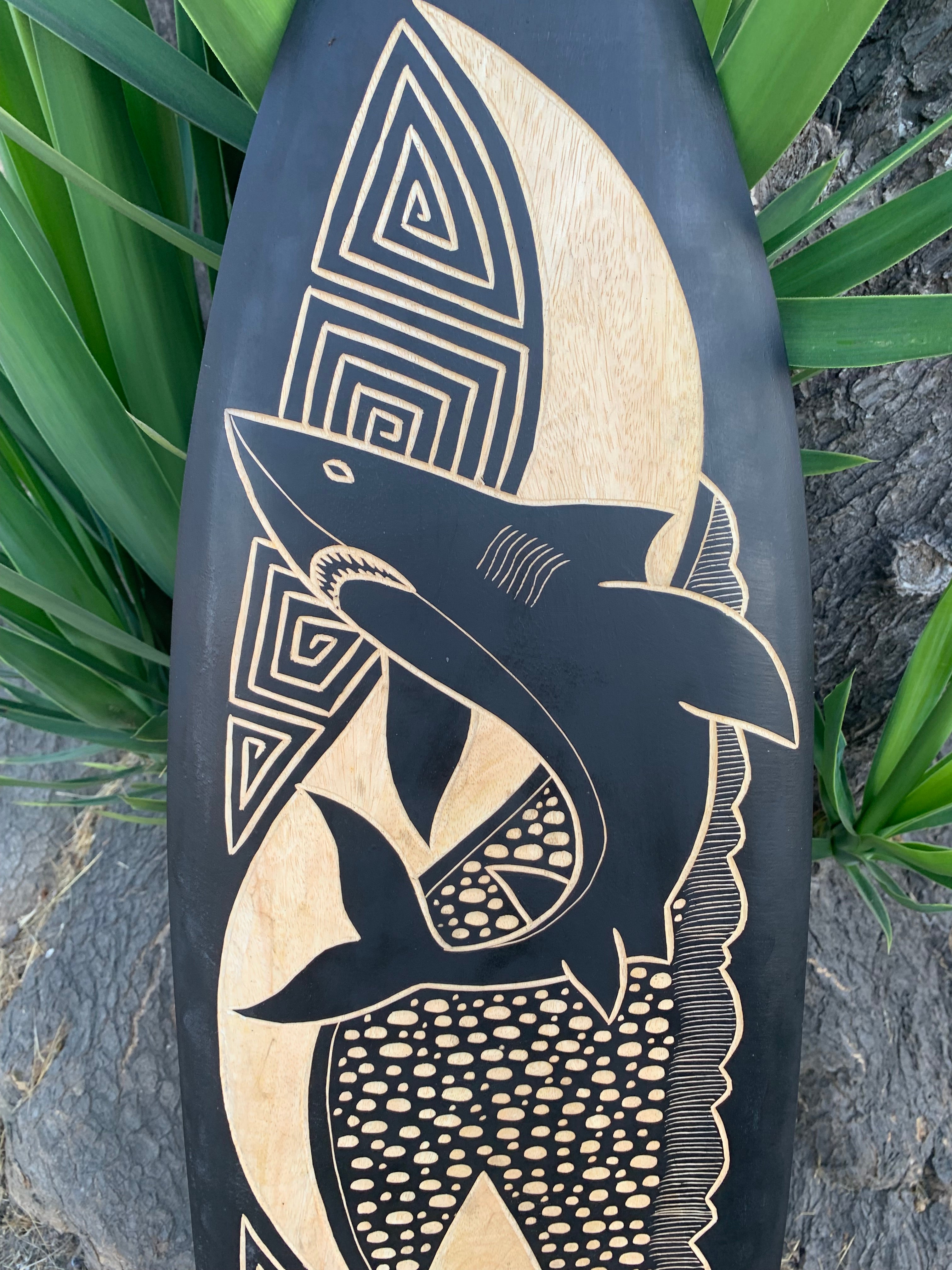 Polynesian-style dolphin carving on a wooden surfboard with geometric spirals