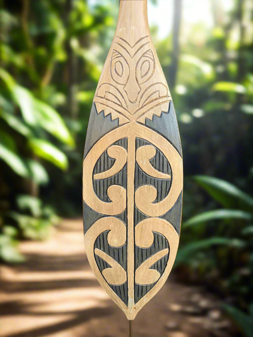 Polynesian-inspired carved wooden paddle with swirling motifs and natural wood tones
