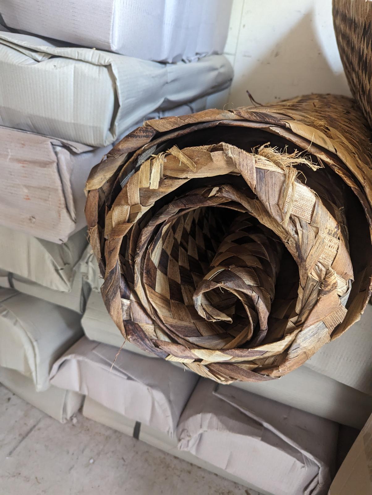 Rolled brown woven reed mat in storage with cardboard boxes nearby