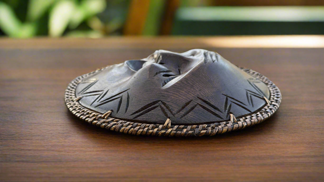 Round black carved object with braided edge and zigzag pattern on a wooden table