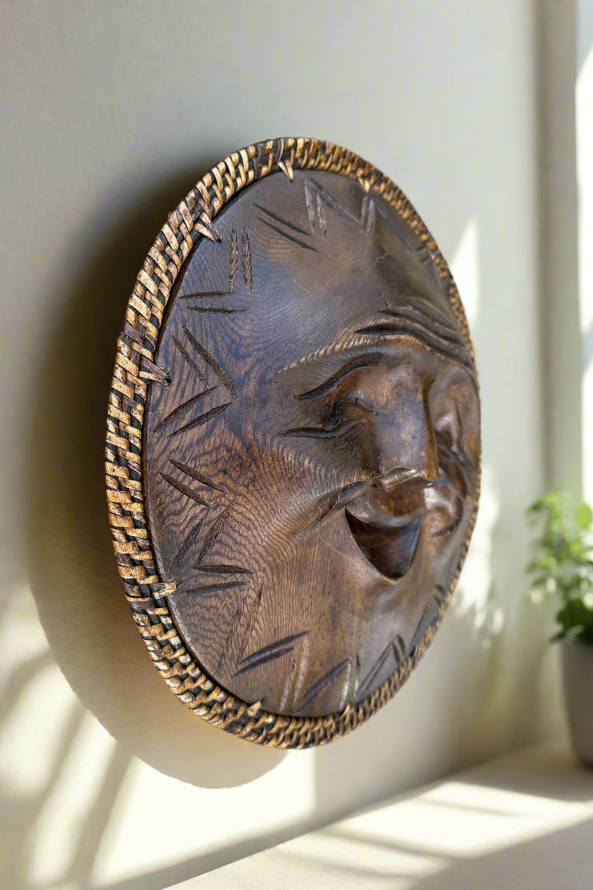 round bronze carved mask with a smiling face and braided border mounted on a wall