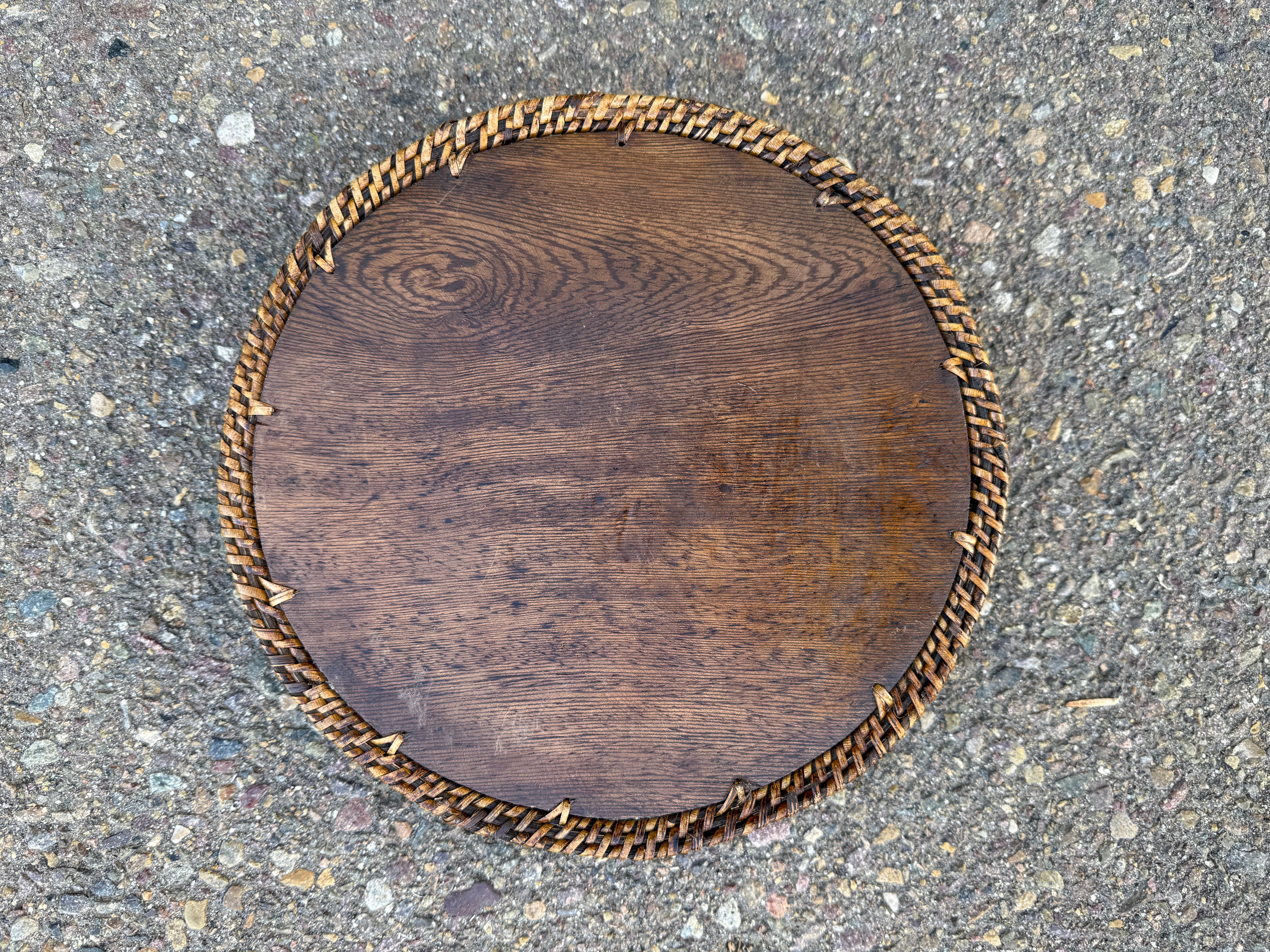 Top view of a round wooden table with a woven wicker edge on a rough stone surface