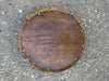 Top view of a round wooden table with a woven wicker edge on a rough stone surface
