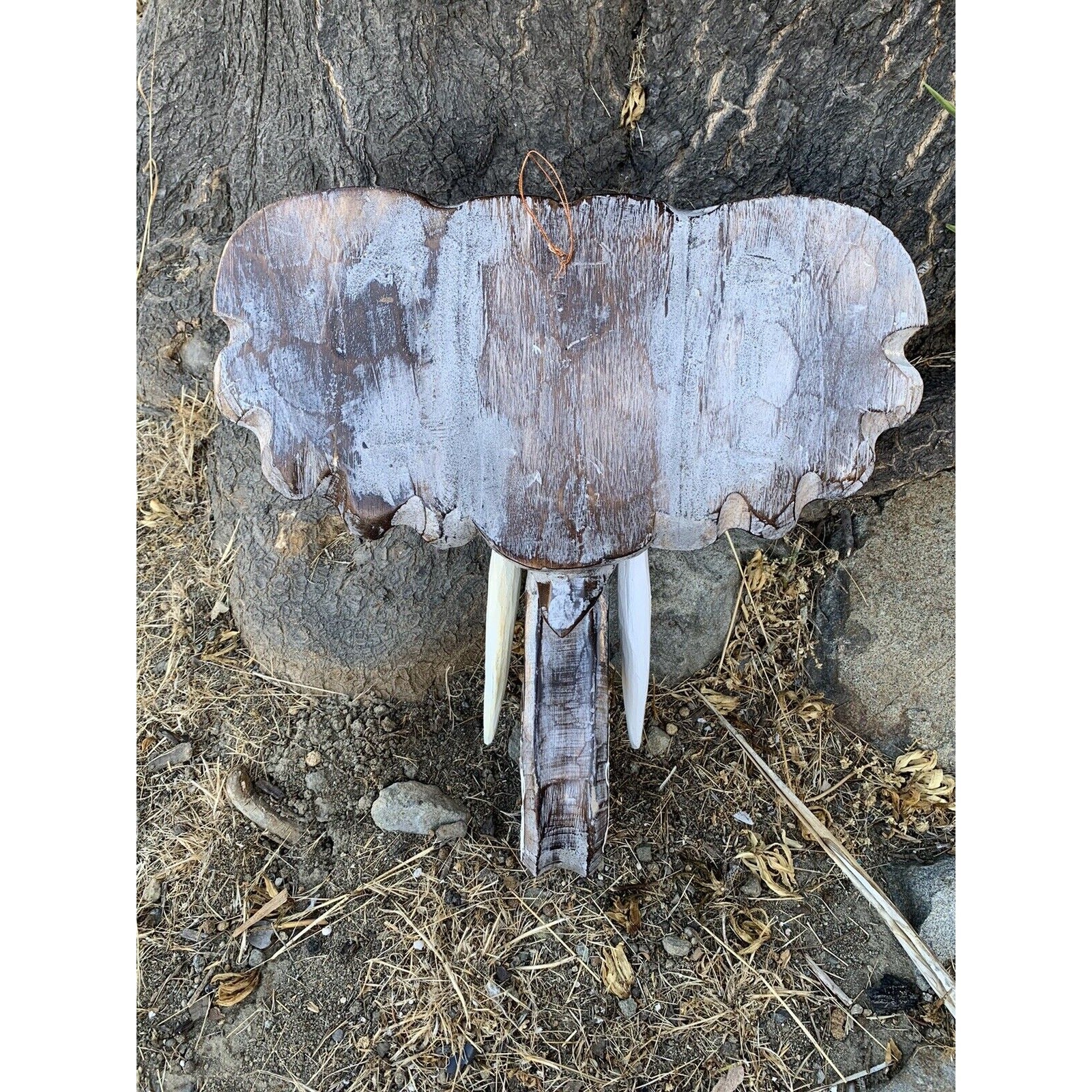 Rustic wooden sign resembling a mammoth head with tusks mounted on a tree trunk.