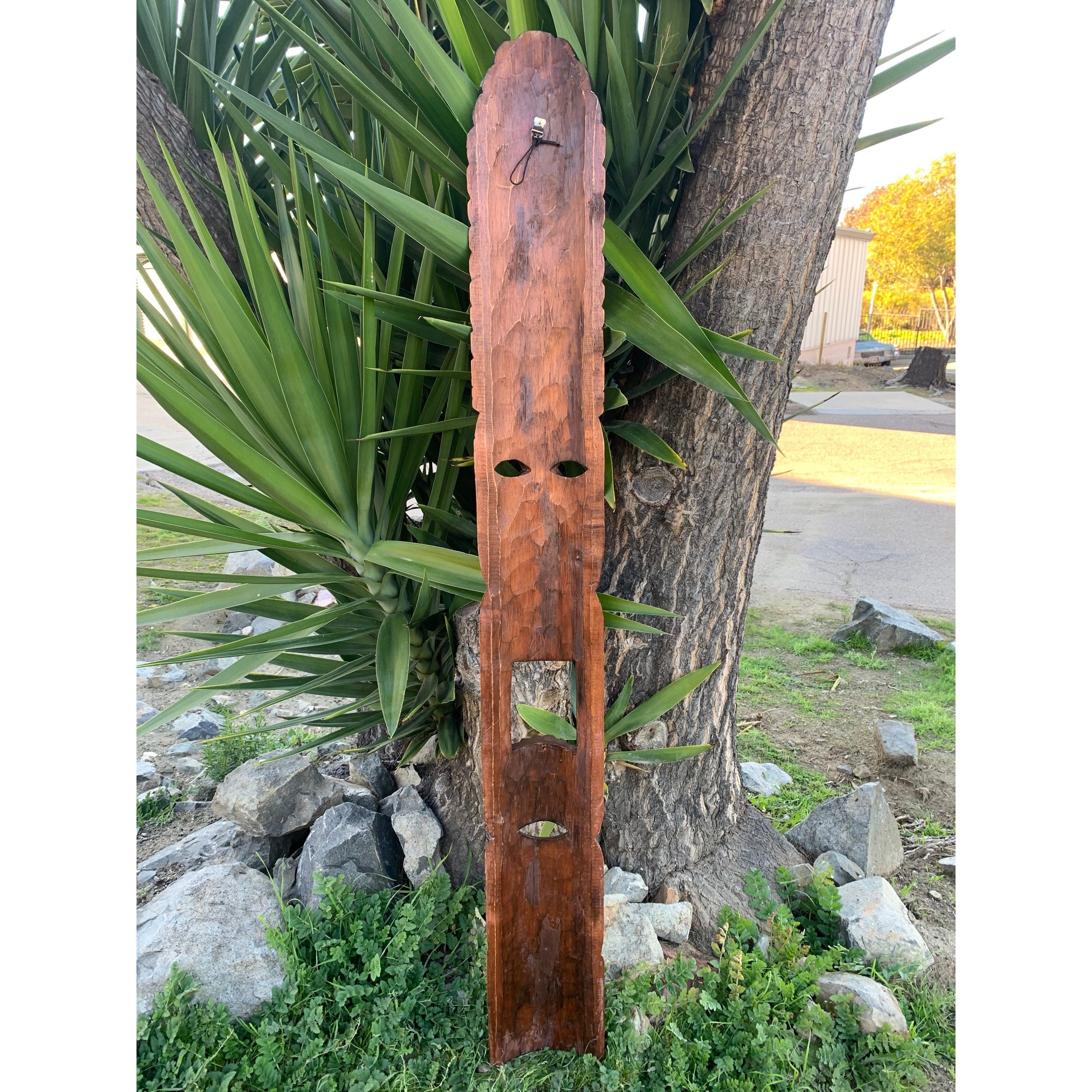 Rustic wooden post with oval cutouts leaning against a tree in a garden