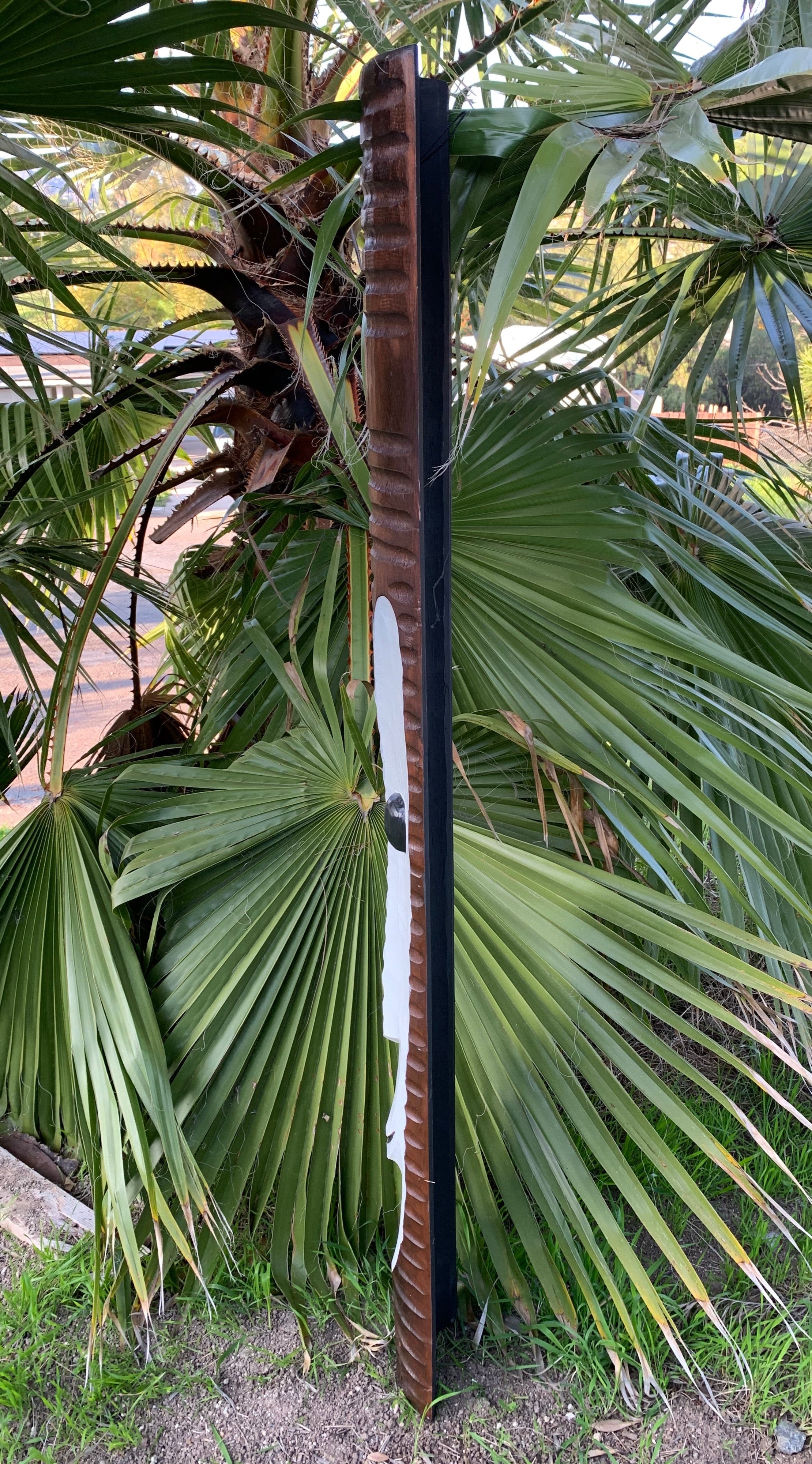 Rusty vertical metal post next to large palm leaves in a garden scene