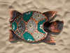 Decorative turtle mosaic on sand with teal and gray pebble sections and shell patterns.