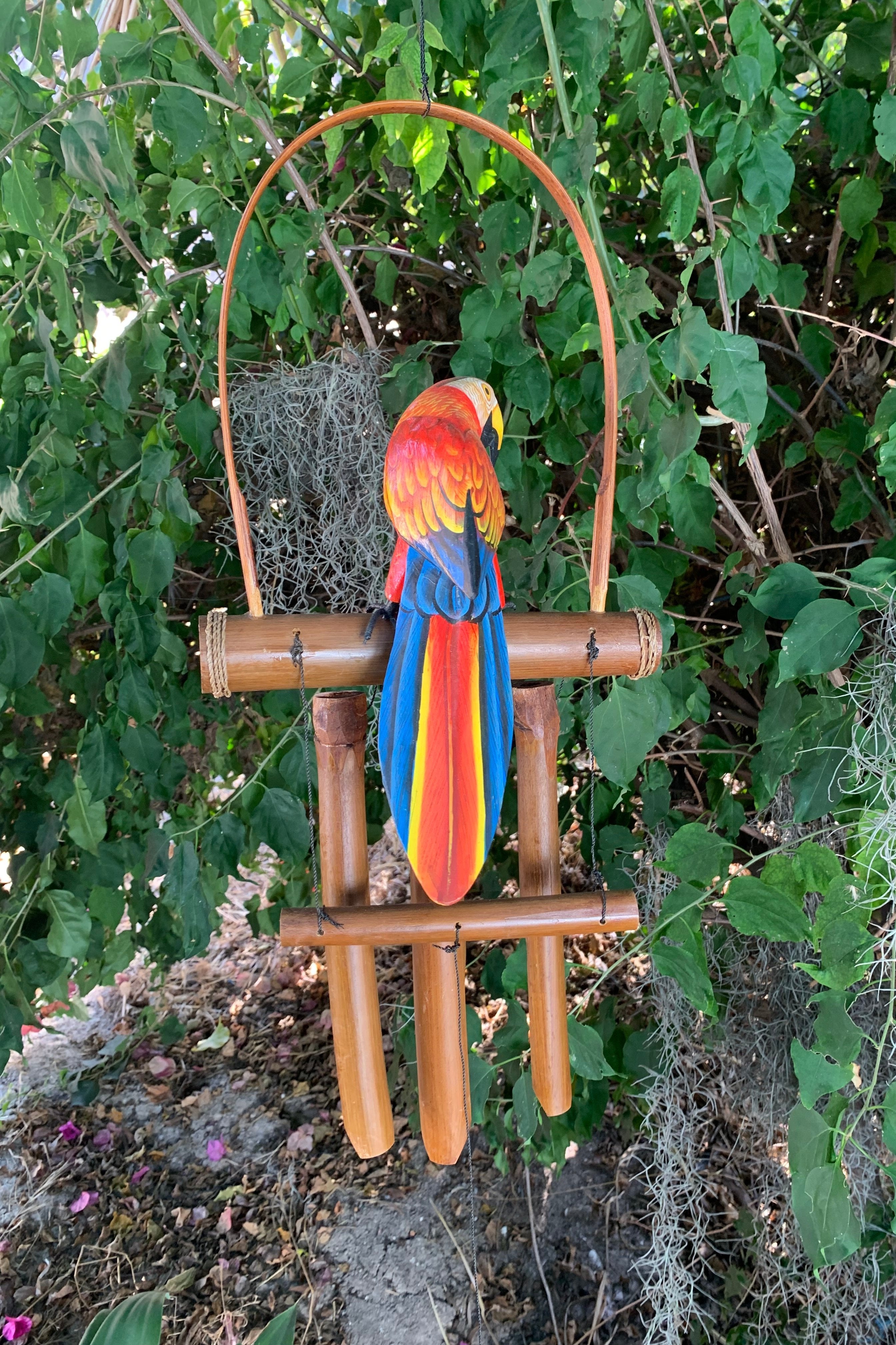 Scarlet macaw perched on a wooden bamboo wind chime in a garden.