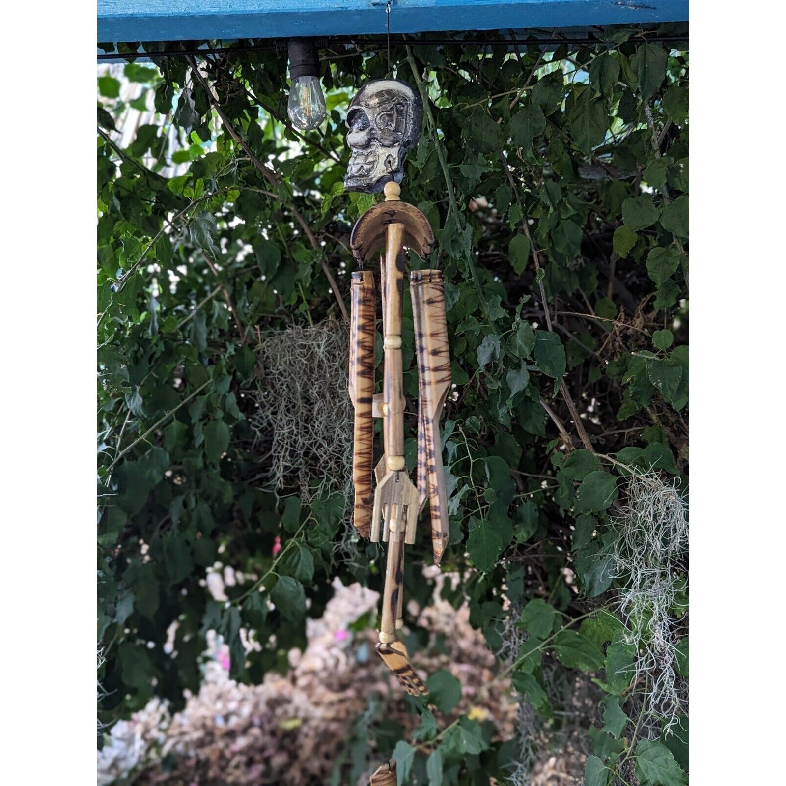 Hanging bamboo wind chime with a skeletal skull topper and light bulb among green vines