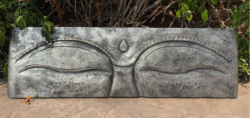 Rectangular stone relief with closed eyes and a central forehead dot, resembling a meditating Buddha.