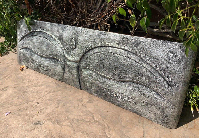 Stone relief panel featuring two closed eyes and decorative swirls in an outdoor setting