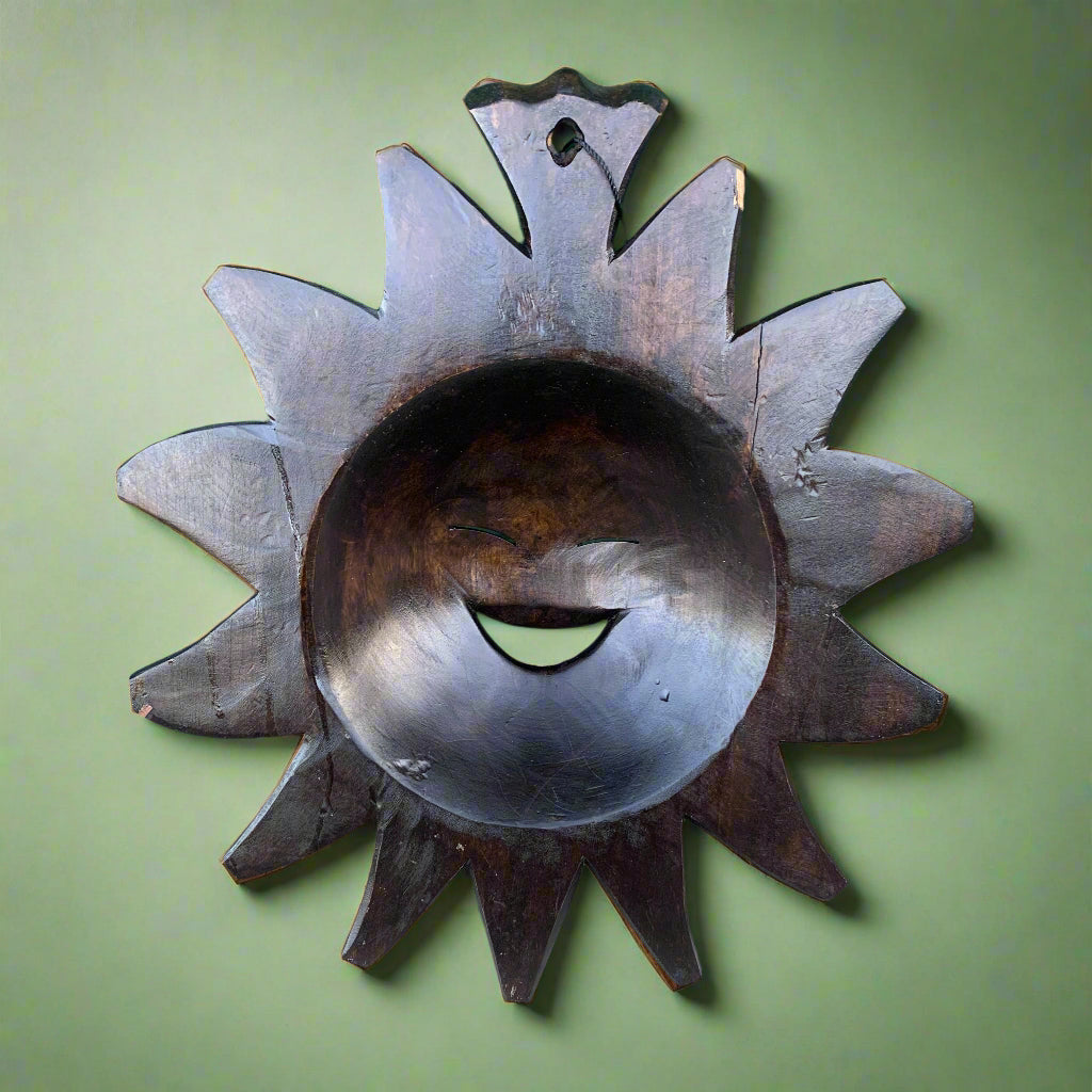Dark wooden sunburst wall decor with a hollow circular center on a green wall.