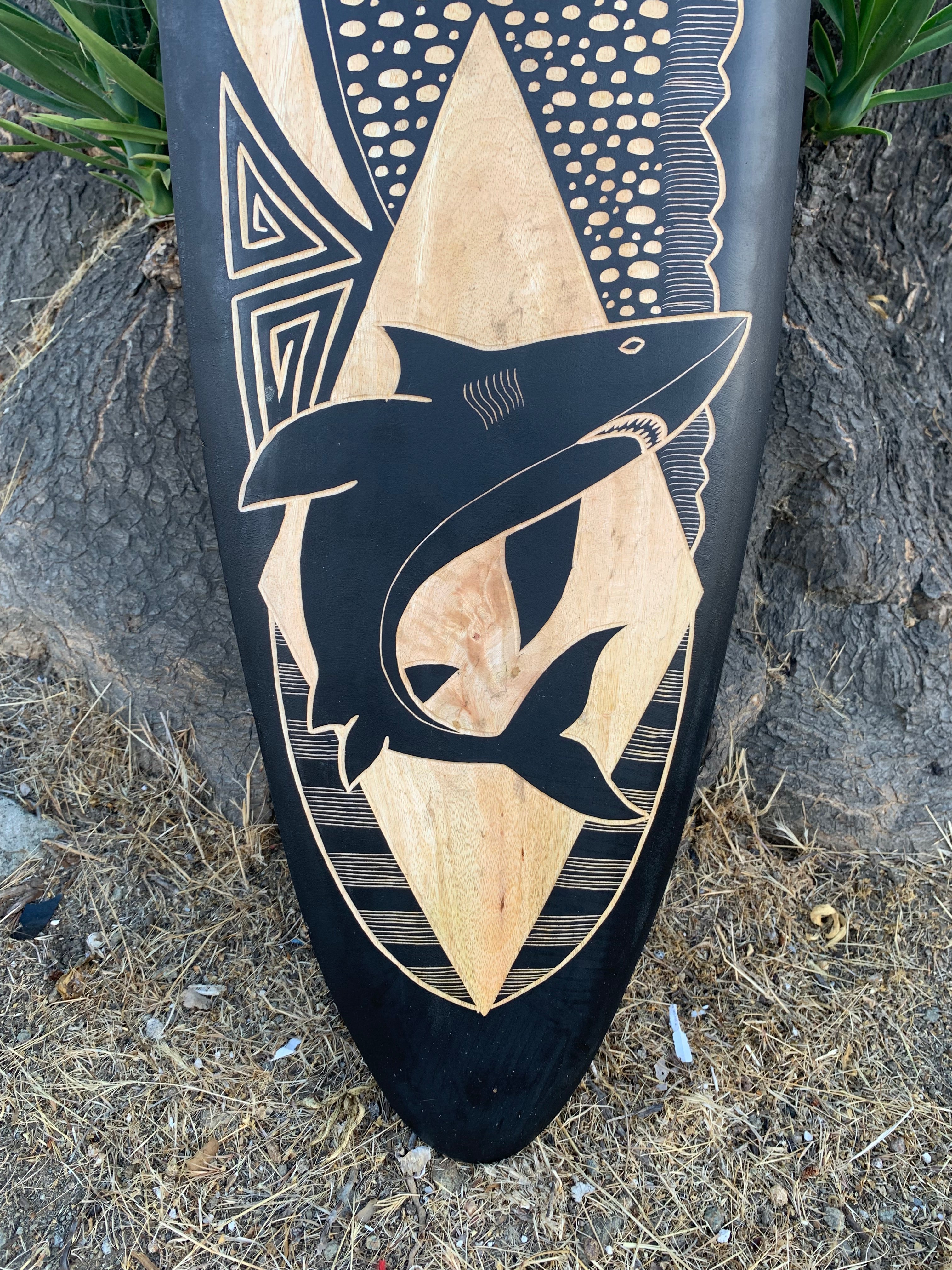 Surfboard featuring a black shark silhouette with wood-toned geometric diamonds and patterns on a dark background