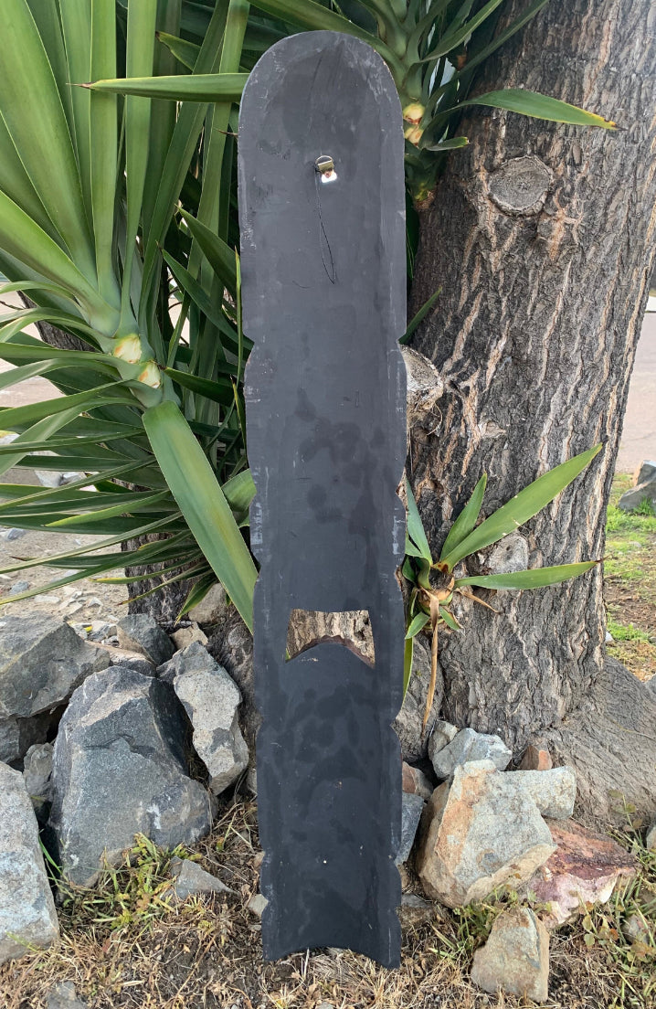 Tall black metal signboard leaning against a tree outdoors