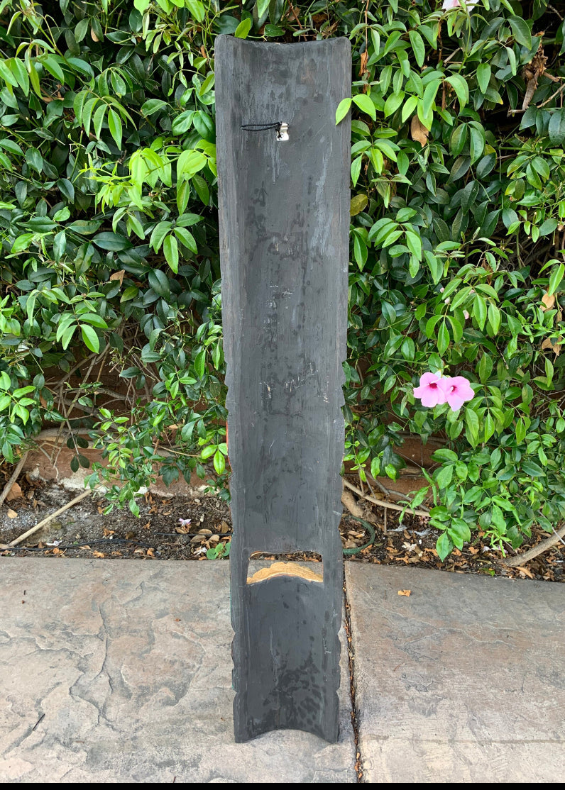 Tall black slate outdoor water fountain with a small faucet in a garden.