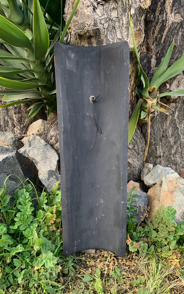 Tall black slate signboard with a rope hanger leaning against a tree in a garden