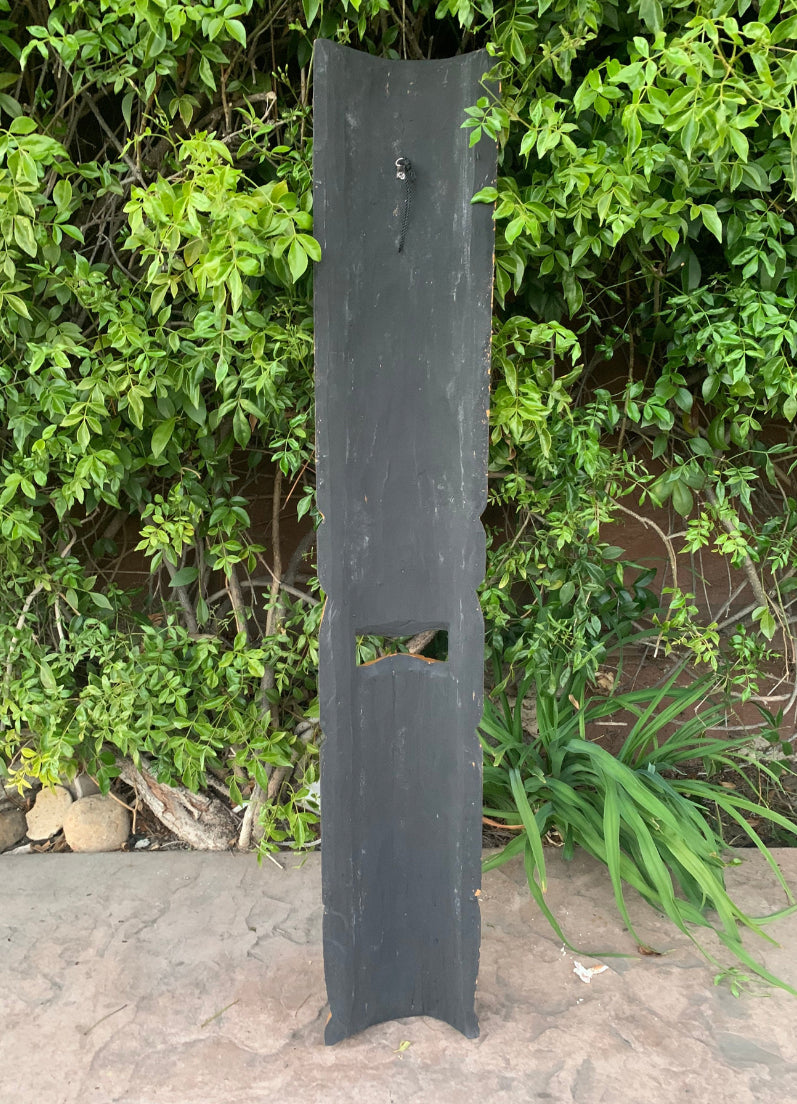 Tall black slate slab with a rectangular cutout standing in a garden.