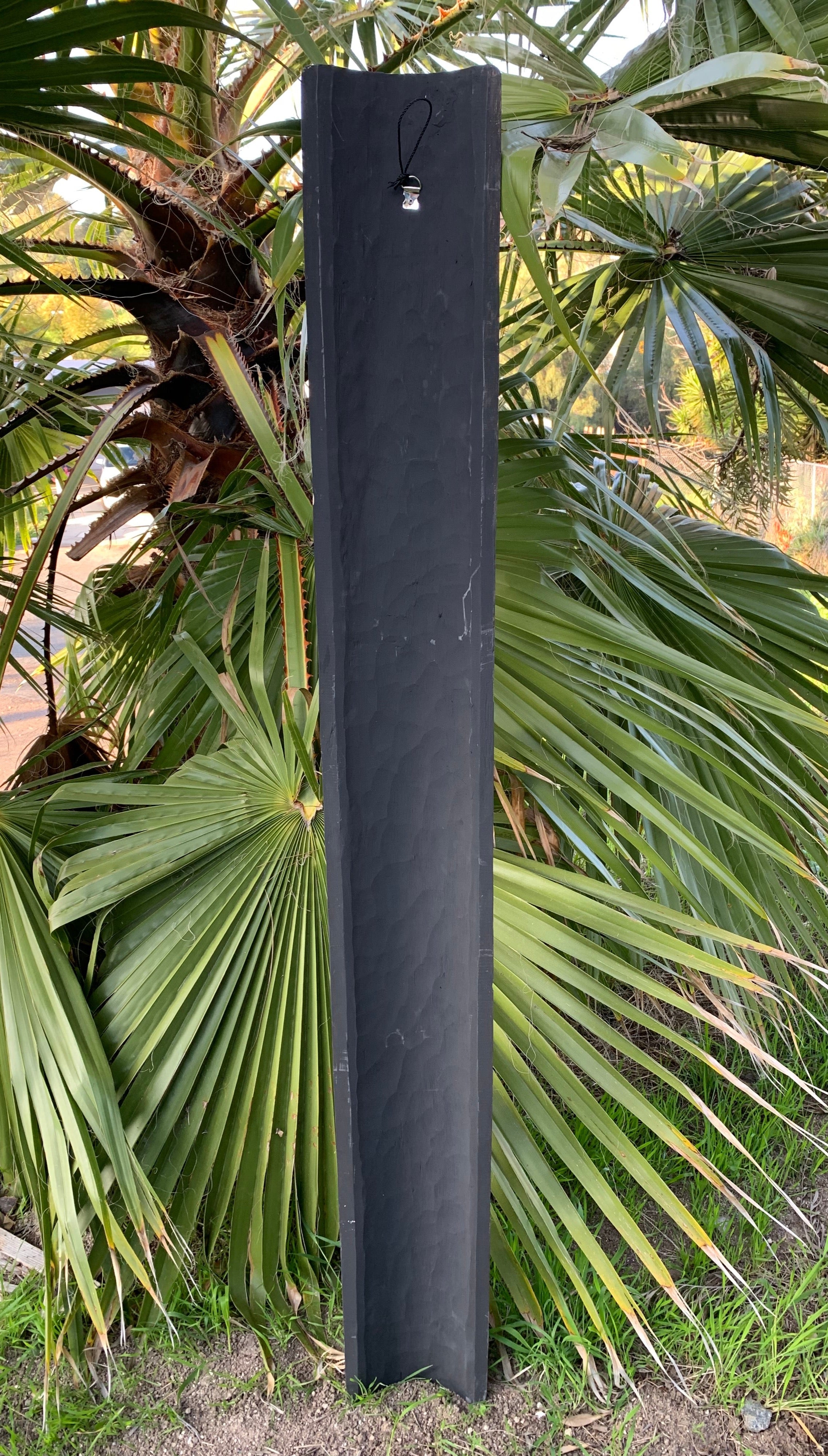 Tall black wooden post standing among palm leaves in a garden