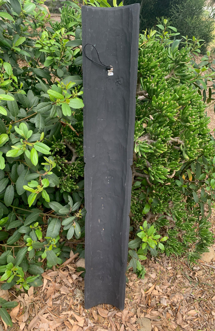 tall dark slate garden post with a hanging tag beside green shrubs