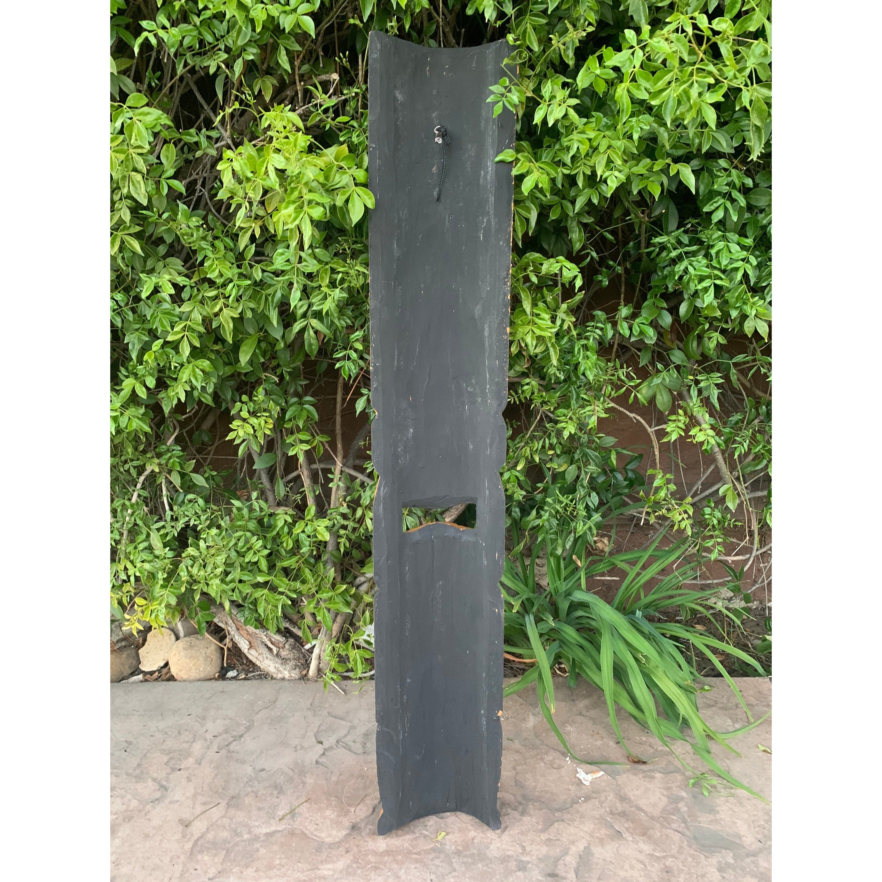 tall dark weathered wooden post with a rectangular cutout on a stone patio with ivy in the background