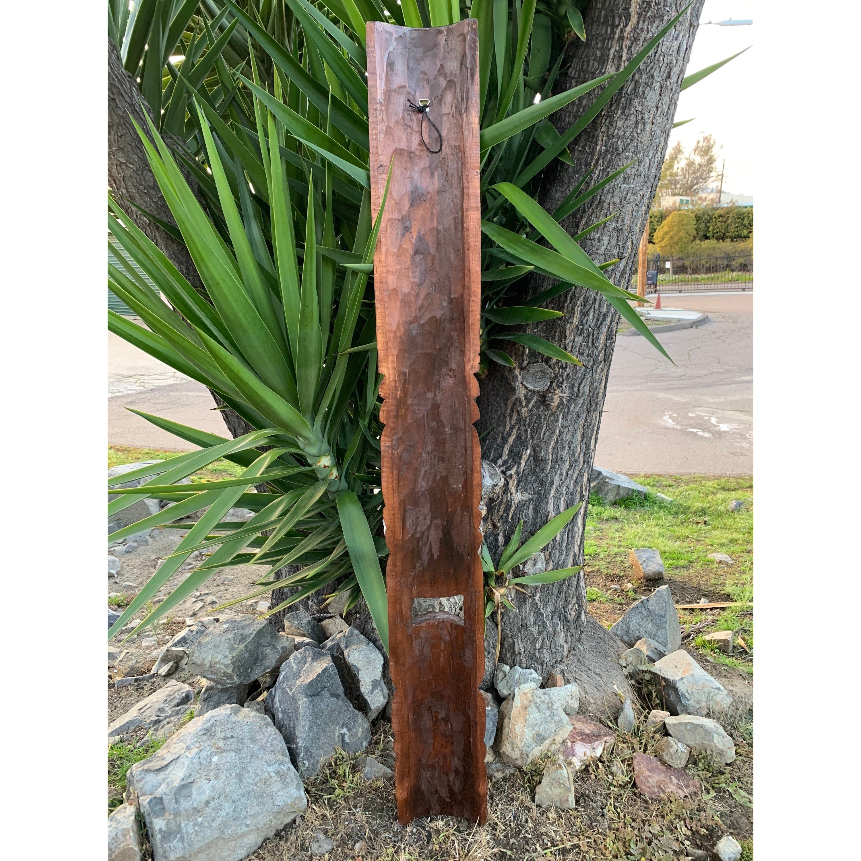 Tall weathered wooden post with carved edges leaning against a tree in a rocky garden