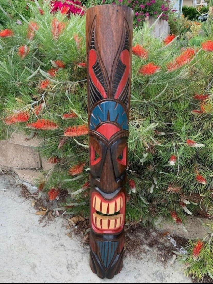 tall wooden totem pole with red and blue face carving in a garden