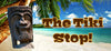 Stone tiki statue on a tropical beach with palm trees and turquoise water, The Tiki Stop! text overlay.