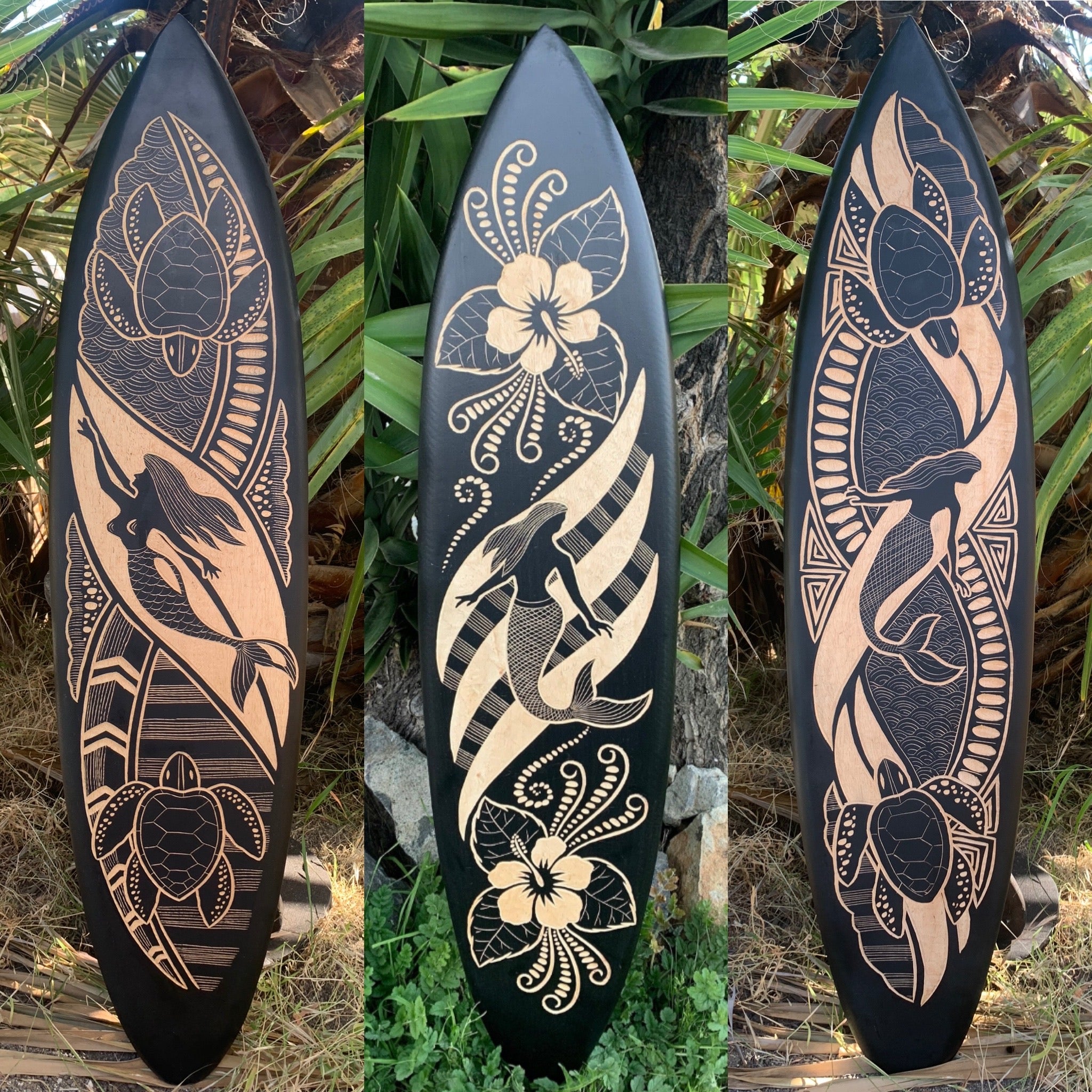 Three black surfboards with tan Polynesian-style carvings featuring dolphins, a sea turtle, and hibiscus flowers.