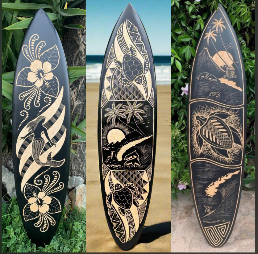 Three black surfboards with beige Polynesian carvings featuring floral motifs, sea turtle, and tropical island scenes.