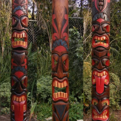 Three red-and-black tiki totem poles with carved faces in a garden.
