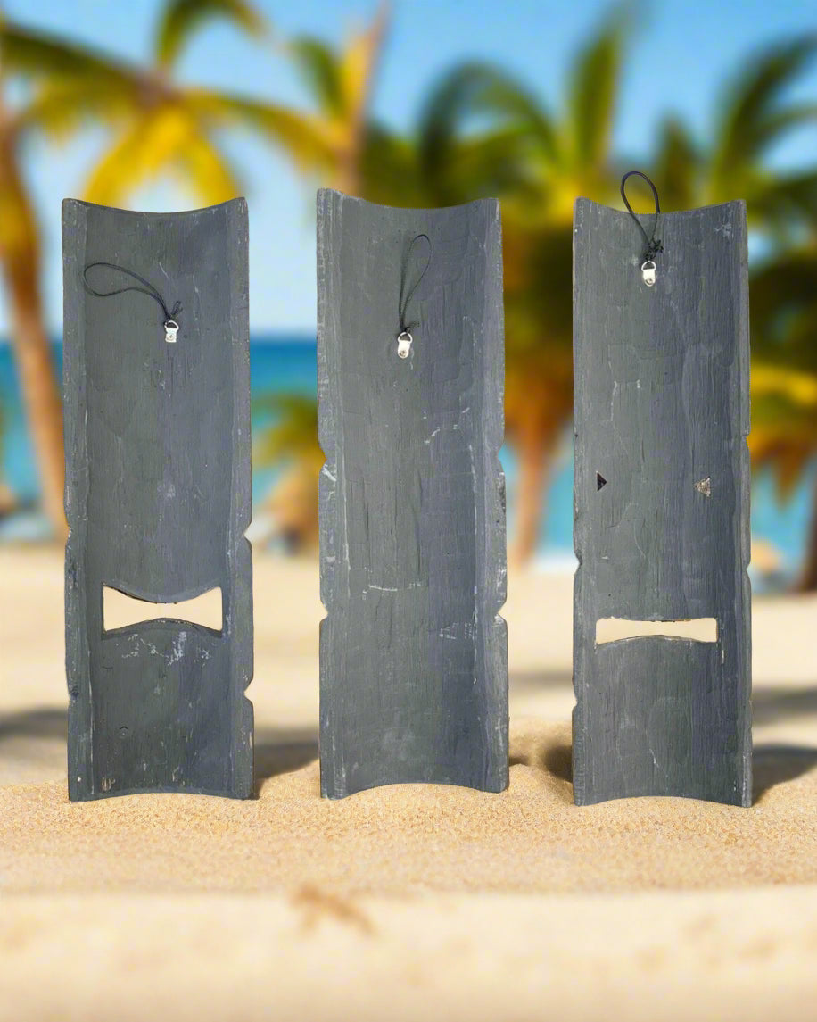 Three tall slate boards with small hanging charms on a sunny beach