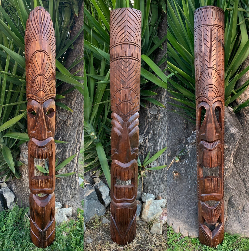 Three tall wooden tiki totem statues with carved geometric patterns outdoors in a garden.